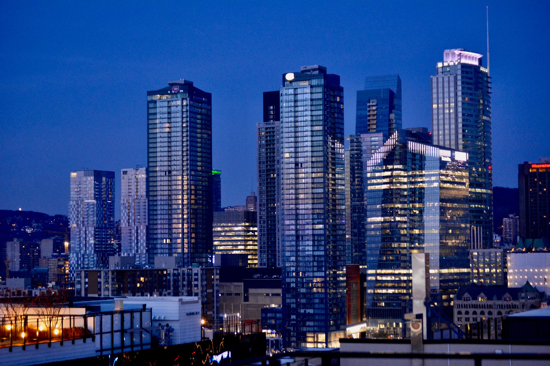 Twilight view of Montreal's illuminated skyline featuring modern skyscrapers against a blue evening sky.